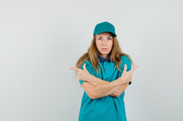 Delivery woman in t-shirt, cap pointing away while crossing arms and looking sensible 