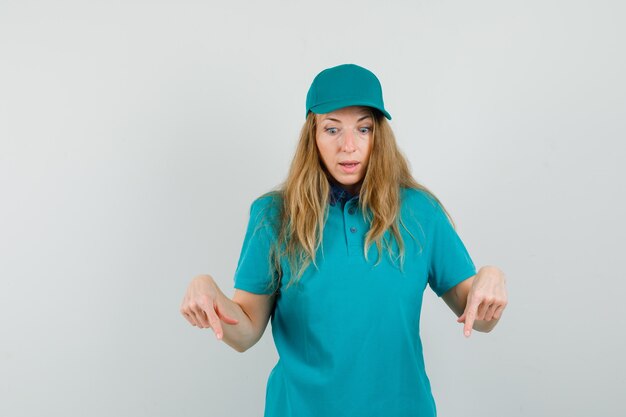 Delivery woman in t-shirt, cap pointing down and looking puzzled 