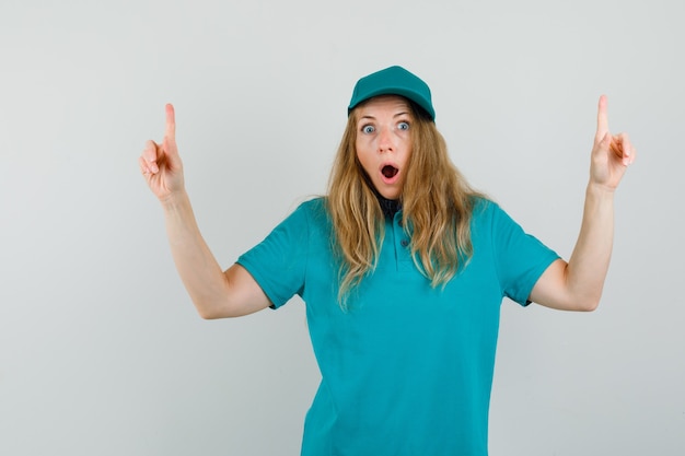 Free photo delivery woman in t-shirt, cap pointing up and looking scared