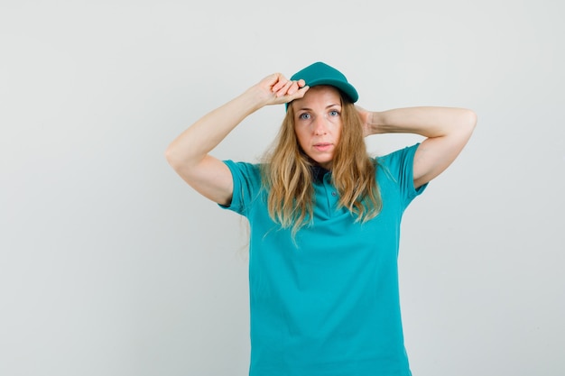 Delivery woman in t-shirt, cap posing while holding her cap 