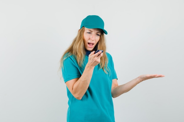 Delivery woman in t-shirt, cap talking into cellphone while shouting 