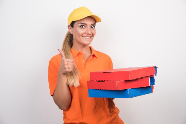 Delivery woman with yellow hat holding pizza boxes and making thumbs up.