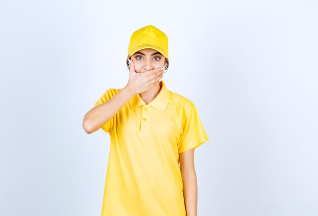 Free photo delivery woman in yellow uniform covering mouth with hand.