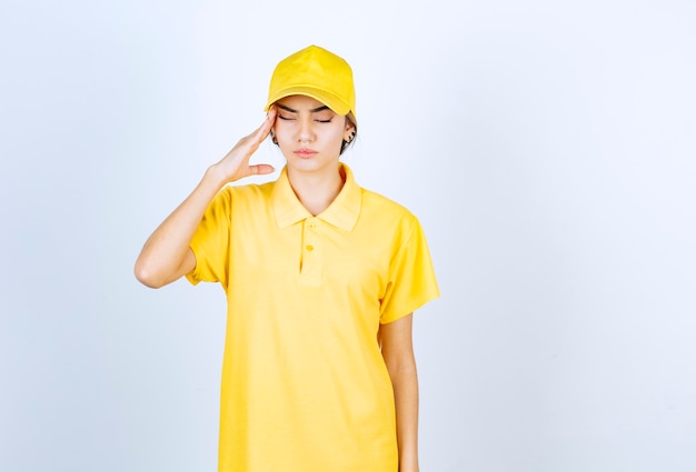 Delivery woman in yellow uniform holding head with closed eyes.