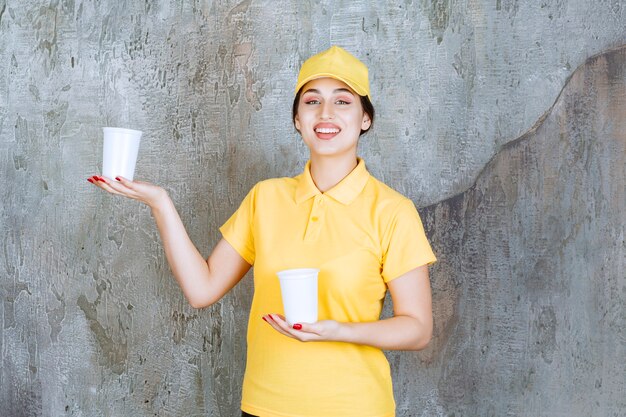 黄色い制服を着た出産の女性が2杯のプラスチック製の飲み物を持って、1つを他の人に渡します。