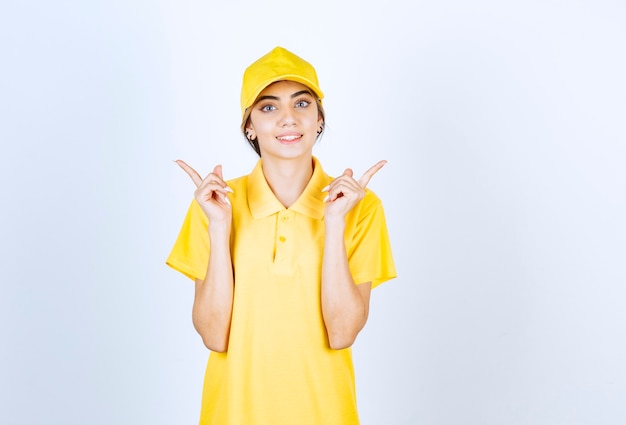 Delivery woman in yellow uniform pointing up with index fingers .