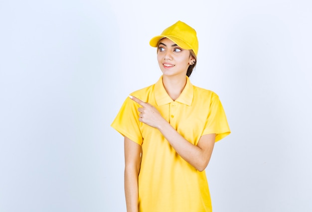 Delivery woman in yellow uniform standing and pointing away with an index finger .