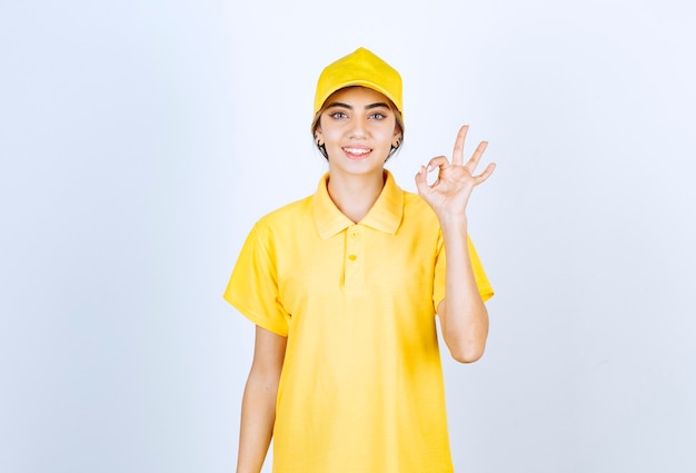 노란색 제복을 입은 배달 여성이 서서 확인 제스처를 보여줍니다.