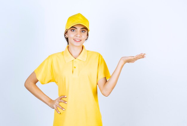 Free photo delivery woman in yellow uniform standing and showing opened palm .