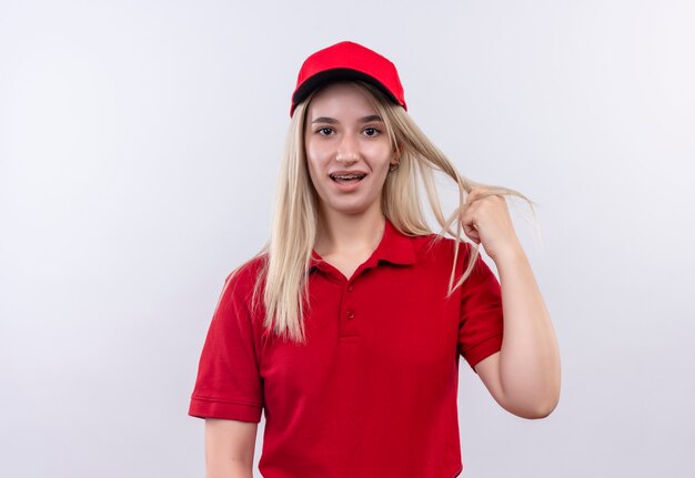 치과 중괄호에 빨간 티셔츠와 모자를 쓰고 배달 젊은 여자는 격리 된 흰 벽에 머리를 잡고