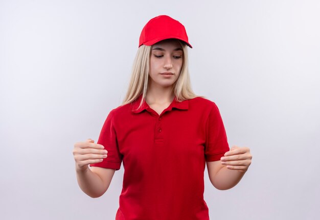 Доставка молодая женщина в красной футболке и кепке притворяется, что держит что-то на изолированной белой стене
