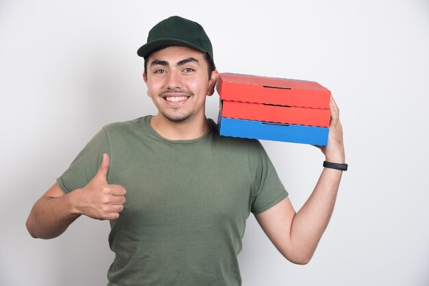 ピザの3つのボックスを保持し、白い背景に親指を表示している配達員。