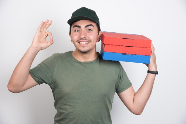 Deliveryman making ok sign and holding pizza boxes on white background.