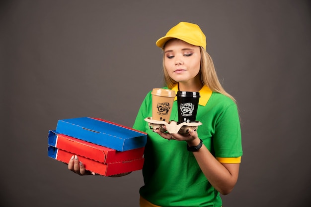 Deliverywoman looking on cups of coffee and holding cardboards of pizza.