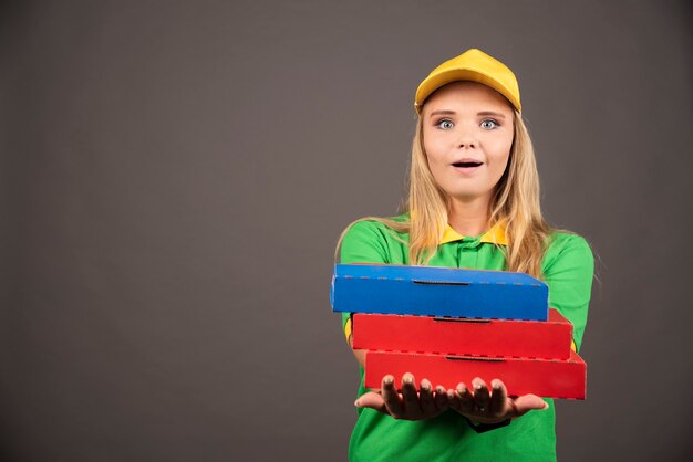 Deliverywoman in uniform giving cardboards of pizza .