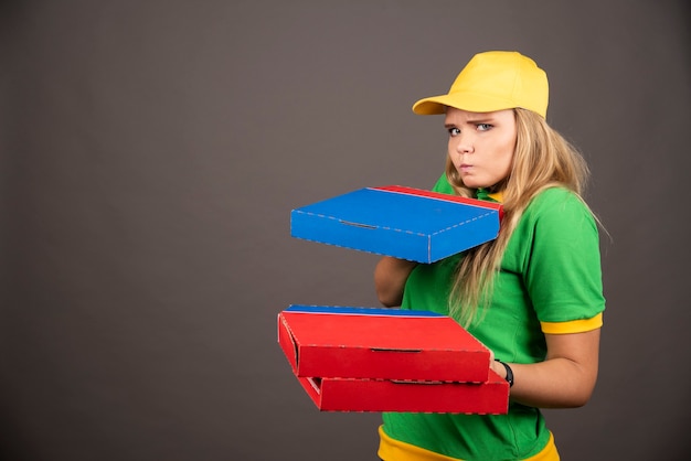 Deliverywoman in uniform holding cardboards of pizza .