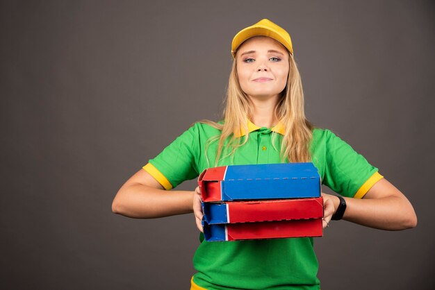 Deliverywoman in uniform holding cardboards of pizza .