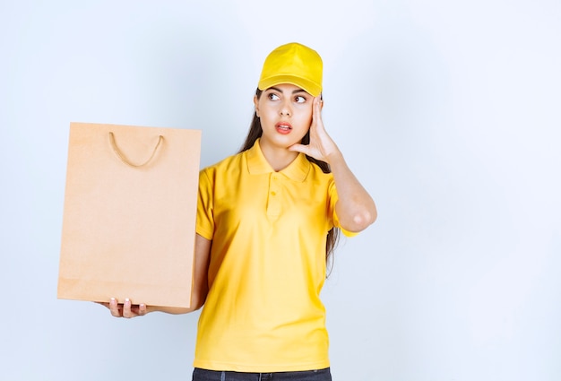 Deliverywoman in yellow cap holding brown craft paper and holding her face.
