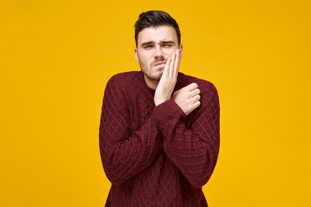 Dental care, dentistry and stomatology concept. Portrait of stressed upset young guy having toothache or sore gum, pressing hand against his cheek,