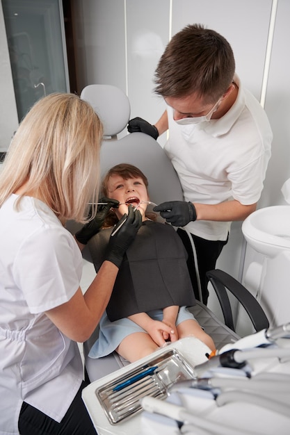 Dentist and assistant examining little girl teeth in dental office