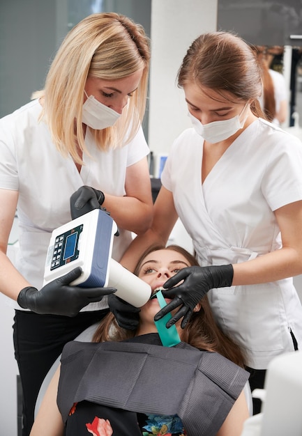 치과 엑스레이 기계로 환자의 치아를 검사하는 치과 의사 및 조수