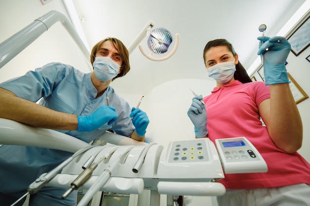 Стоматолог и помощник позирует со своими инструментами