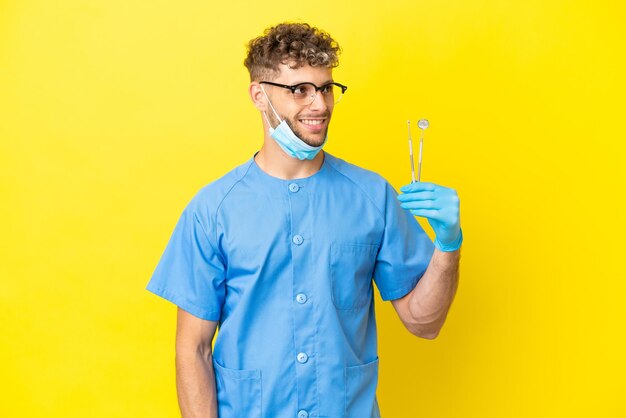 Dentist blonde man holding tools isolated on background thinking an idea while looking up