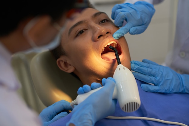 Dentist curing Asian male patient's tooth filling with ultraviolet light 