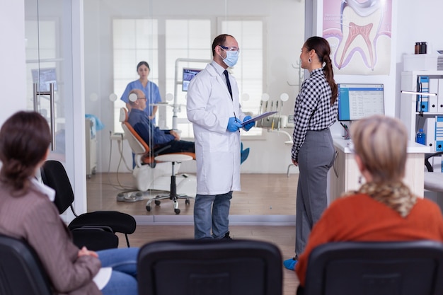 Dentist doctor interrogating woman and taking notes on clipboard standing in waiting area