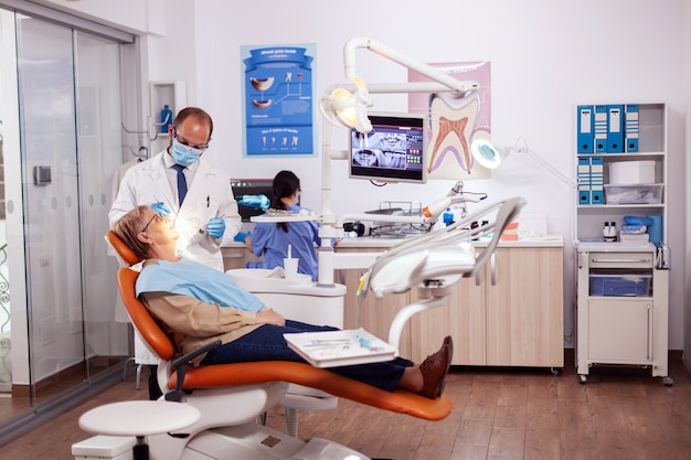 歯科治療と介入を行う歯科医。年配の女性に。オレンジ色の機器を備えた歯科医院の歯科医による診察中の高齢患者。