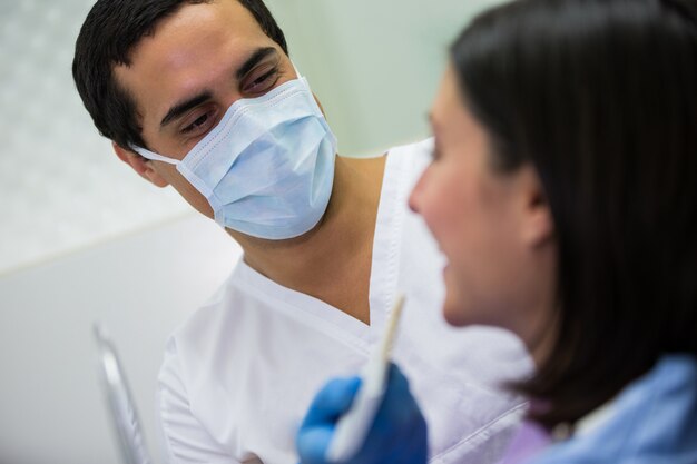 Dentist examining female patient with model of teeth shades