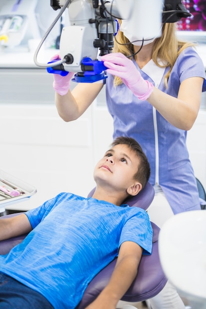 Foto gratuita dentista esaminando i denti di un ragazzo attraverso il microscopio