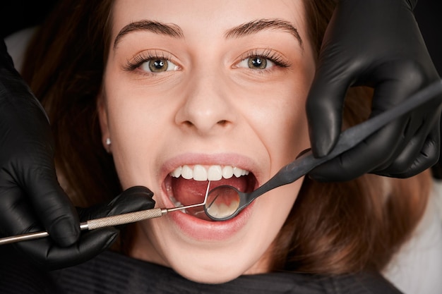Руки дантиста в стерильных перчатках осматривают женские зубы