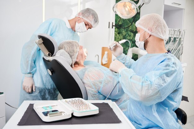 Стоматолог и его ассистент, работающие с пациентом в стоматологическом кресле в кабинете стоматолога