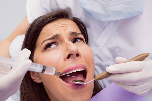 Dentist injecting anesthetics in scared female patient mouth