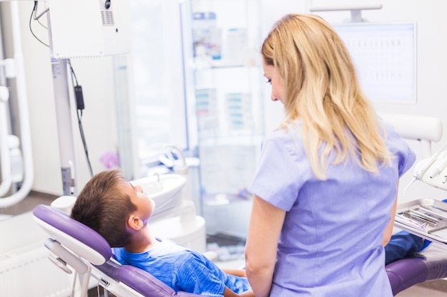 Dentist looking at boy sitting on dental chair in clinic