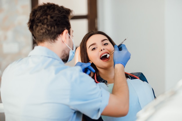 歯科医院で綿の女性の若い患者と一緒にプロの歯のクリーニングをしている歯科医。