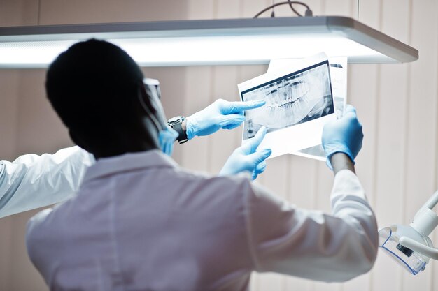 Стоматологический кабинет и концепция врачебной практики Профессиональный афроамериканский врач в стоматологии указывает на зубы Xray