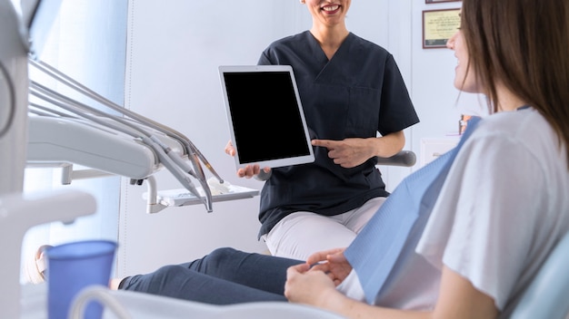 Dentist pointing on digital tablet screen to female patient sitting on chair
