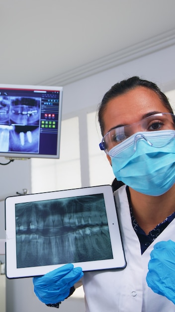 患者と一緒にそれをレビューしている錠剤の歯のX線写真に表示されている歯科医。現代の口腔病クリニックで一緒に働いている医師と看護師が、ノートブックディスプレイを使用して歯の老婆X線撮影を説明します