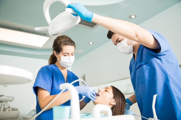 Foto gratuita dentista che cura il paziente con uno strumento dentale mentre un collega maschio regola la luce in clinica