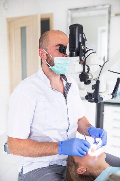 Стоматолог, использующий стоматологический микроскоп для лечения зубов женских пациентов