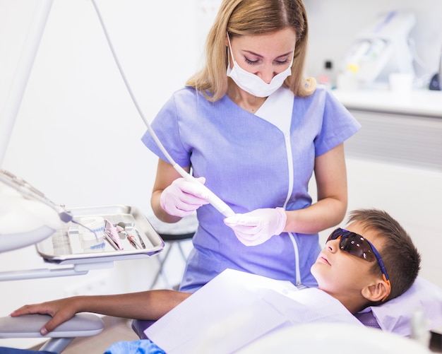 歯科医は超音波スケーラーを使って診察室の少年の歯を治療する
