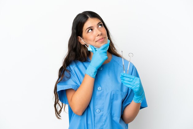 孤立した白い背景の上にツールを保持し、見上げる歯科医の女性