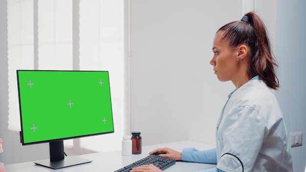 歯科医院で歯のケアのためにコンピューターの水平方向の緑色の画面で作業している歯科医。モックアップテンプレートと孤立した背景のクロマキーでキーボードとモニターを使用している女性 無料写真