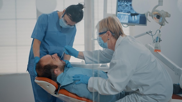 Dentistry team doing teeth consultation to treat patient with toothache, using dental equipment in stomatology office. Dentist and assistant examining denture after drill procedure.