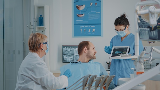 Dentistry team explaining radiography to sick patient, doing oral care examination to cure toothache. Stomatologist and assistant consulting x ray results to do dental drill procedure.