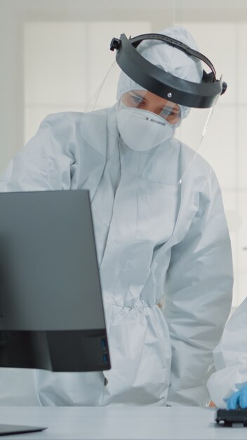 Dentistry team of specialists with ppe suits using computer for modern dental healthcare. Nurse sitting at desk, looking at monitor while dentist analyzing screen during covid pandemic