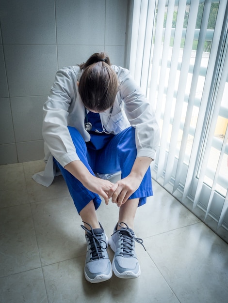 Medico femminile depresso che si siede nella disperazione ad un corridoio dell'ospedale - concetto di dispiacere e di sanità