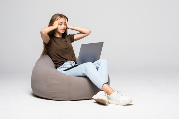 Подавленная и разочарованная женщина, работающая с компьютерным ноутбуком, отчаянно пытается работать, изолированную на белой стене. Депрессия